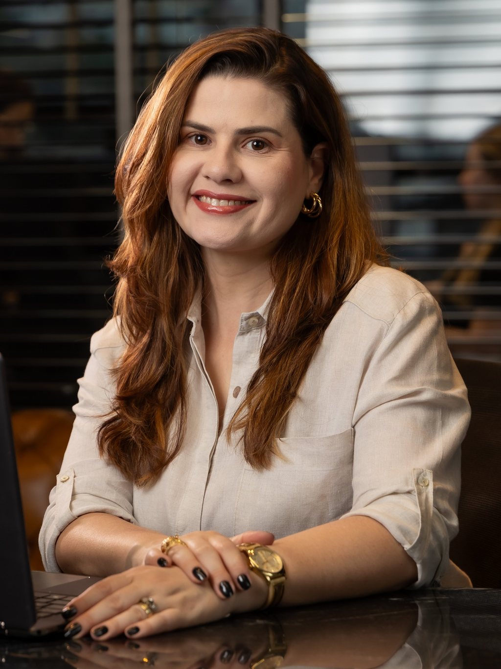 Regina Sardanha, CEO da Ever, sorrindo, sentada à mesa com notebook, vestindo camisa bege
